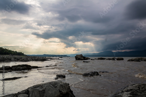 Fleuve sous un ciel gris avec des nuages d'orage et rayon de soleil