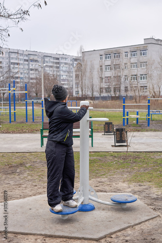 A woman in the early morning is engaged in street simulators. Disc for rotating the waist.