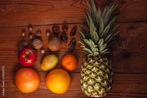 Tropical fruits and nuts vegan diet flatlay. Pineapple  grapefruit  orange  pear  walnuts on wooden background.Healthy weight loss food ingredients.Minimal style.Healthful fats  dietary fiber vitamins