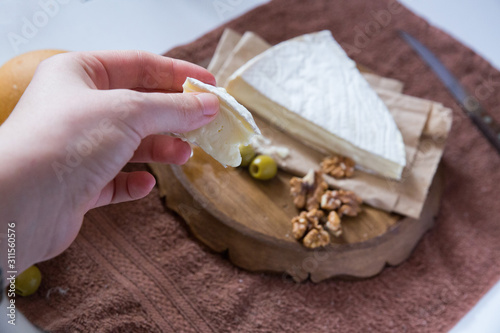 hand holds a piece of cheese on a background of brie cheese, nuts and olives