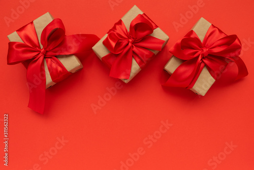 Gift boxes wrapped brown craft paper and red ribbon on red background. Valentines day or Mothers day celebration concept. Top view