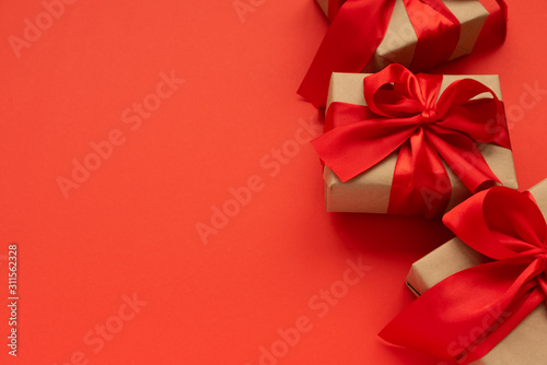 Gift boxes wrapped brown craft paper and red ribbon on red background. Valentines day or Mothers day celebration concept.
