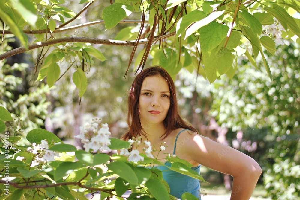Beautiful brunette woman with long hair and blue eyes walking in the blooming park at spring in sunny day with bright sunshines and green trees Beautiful brunette woman with long hair and blue eyes walking in the blooming park at spring in sunny day with bright sunshines and green trees