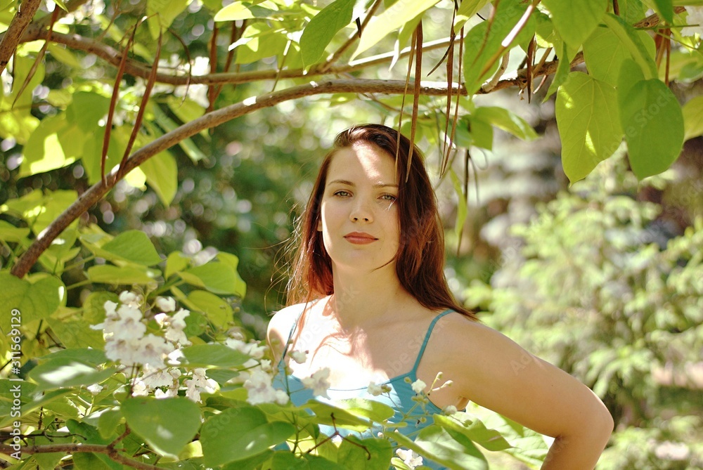 Beautiful brunette woman with long hair and blue eyes walking in the blooming park at spring in sunny day with bright sunshines and green trees Beautiful brunette woman with long hair and blue eyes walking in the blooming park at spring in sunny day with bright sunshines and green trees