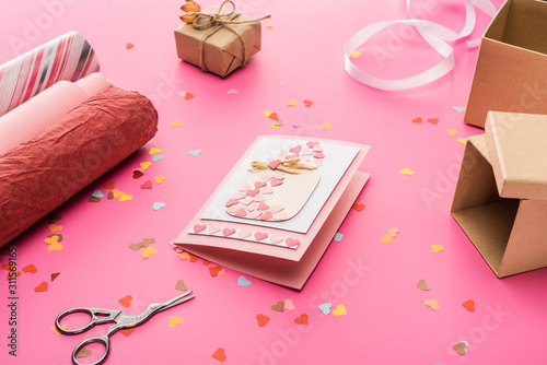 valentines confetti, scissors, greeting card, wrapping paper, gift box on pink background