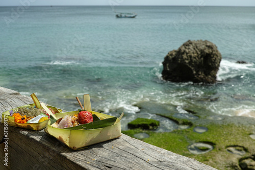 Balinese religious offerings of fruit and incense in front of the tropical coastline