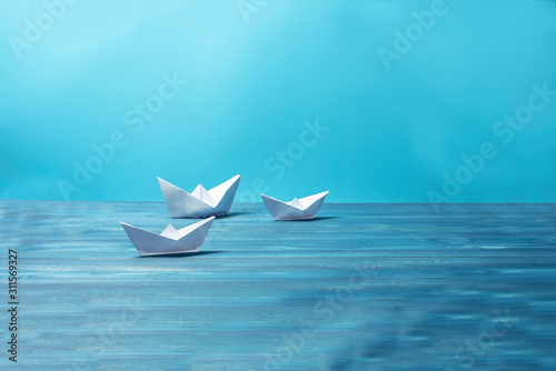 Paper ships on a background in sea tones on a wooden desk. Concept
