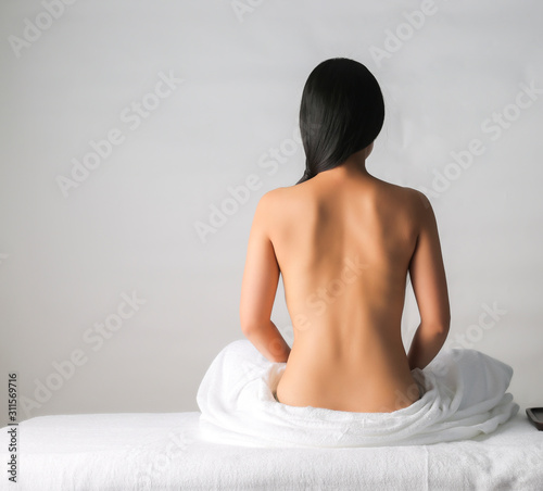 Back view of Asian female sitting on bed waiting for spa massage photo