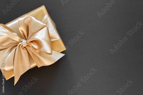 Festive background with gold gift, box with gold ribbon and bow on black background, flat lay, top view,copy space