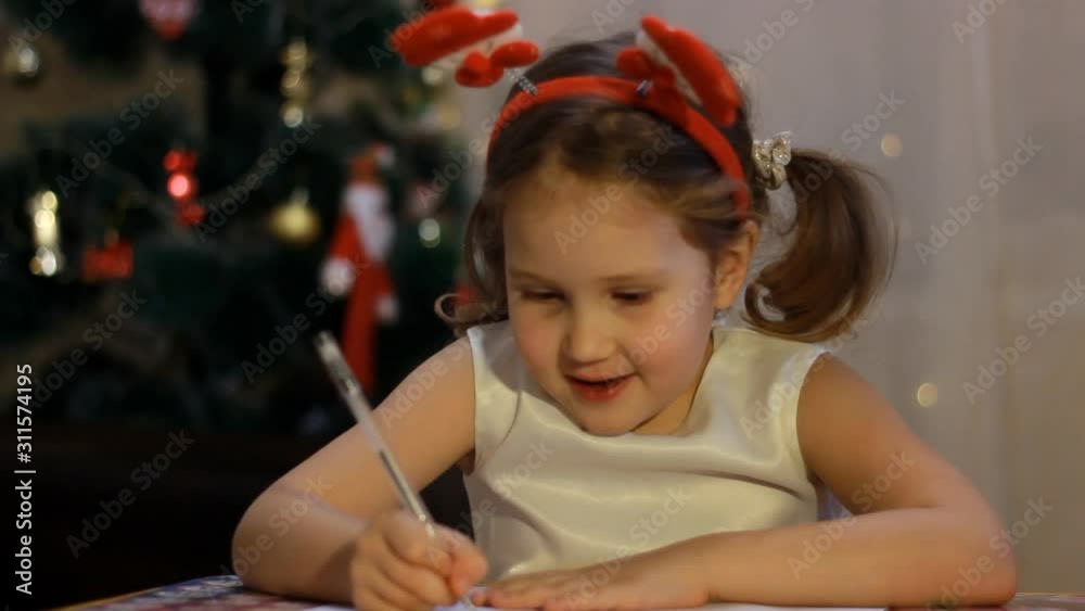Sweet caucasian child is writing a letter to santa claus in room, decorated for christmas, preparing for holiday -christmas spirit, holidays and celebrations concept close up Sweet caucasian child is writing a letter to santa claus in room, decorated for christmas, preparing for holiday -christmas spirit, holidays and celebrations concept close up