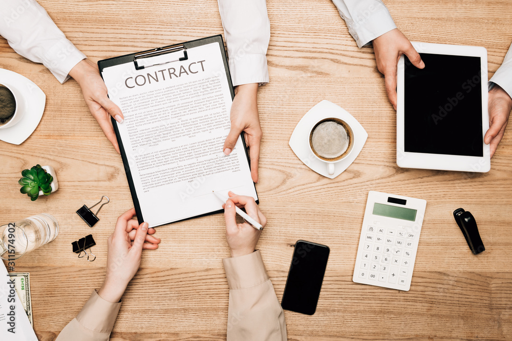 Top view of business partners sign contract with coffee and calculator on table Top view of business partners sign contract with coffee and calculator on table