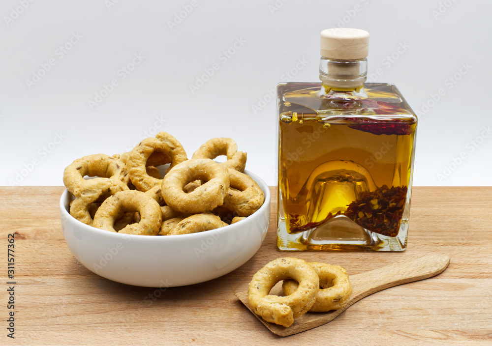 Apulian Taralli with fennel seeds. Extra virgin olive oil with chili pepper. Wooden table, white background. Apulian Taralli with fennel seeds. Extra virgin olive oil with chili pepper. Wooden table, white background.