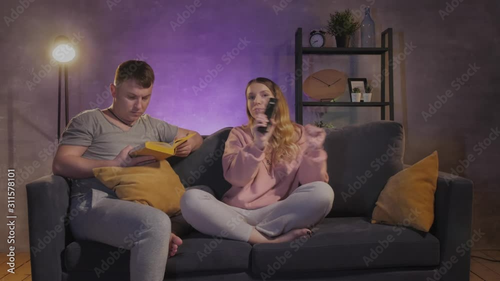 Beautiful girl watching TV. A man reads a book near to his wife Beautiful girl watching TV. A man reads a book near to his wife
