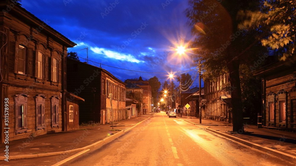 Street with classic wooden houses on both sides of the road at night in Irkutsk, Russia.