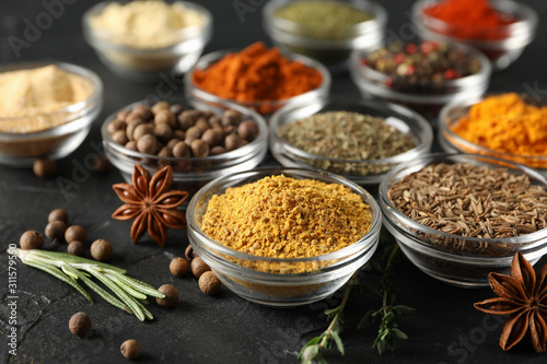 Bowls with different spices and ingredients on black background, close up
