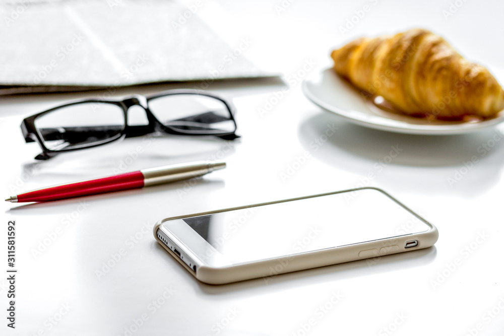 Office breakfast with croissant, phone and newspaper on white desk Office breakfast with croissant, phone and newspaper on white desk