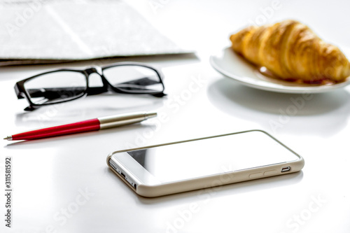 Office breakfast with croissant, phone and newspaper on white desk photo