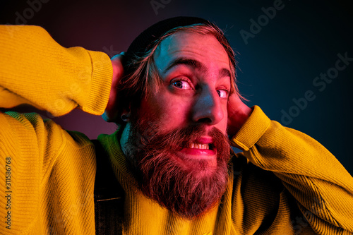 Exremely shocked, astonished. Caucasian man's portrait on gradient studio background in neon light. Beautiful male model with hipster style. Concept of human emotions, facial expression, sales, ad. photo