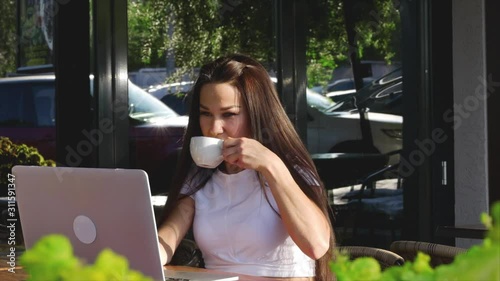 Beautiful Sunny Day Young Woman Drinks Morning Coffee in a Cafe, Making Online a Purchase Easy Payment on the Internet Using a Mobile Phone or Laptop. photo