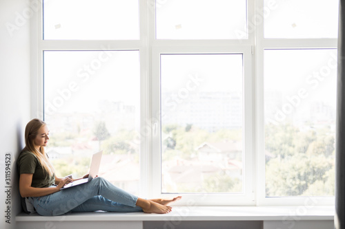 Young pretty girl sitting near the window with a laptop. Free Download Young pretty girl sitting near the window with a laptop. - GFXLoad