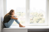 Sad depressed young woman having social problems sitting on windowsill