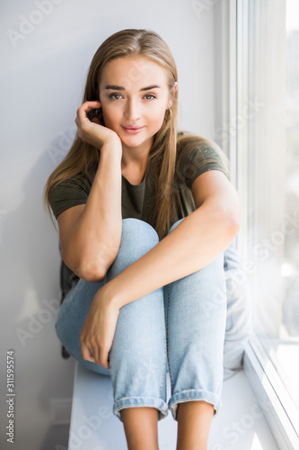 Beautiful young woman sitting at windowsill at home