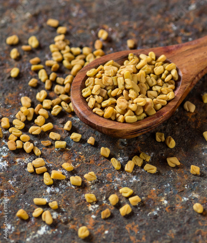 Fenugreek seeds in wooden spoon on textured background photo