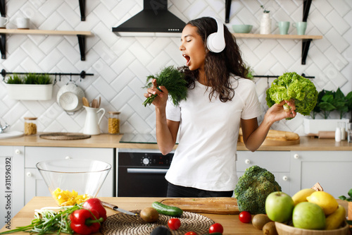 Foto Funny girl in big wireless headphones is singing on imaginary greenery microphon