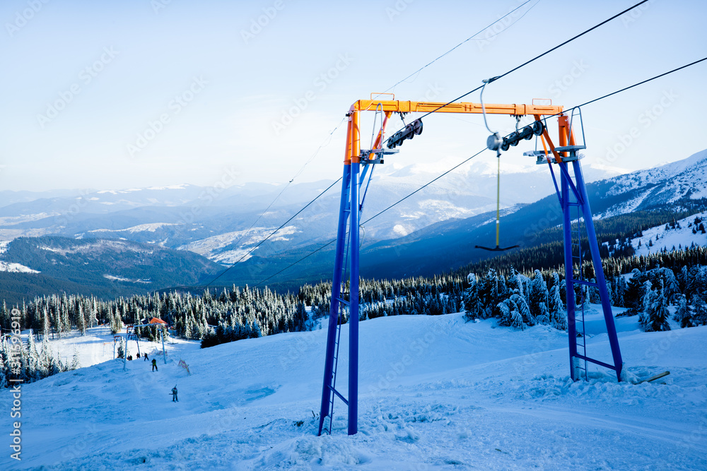 Manual ski lift and some skiers with mountains and valley at background Manual ski lift and some skiers with mountains and valley at background