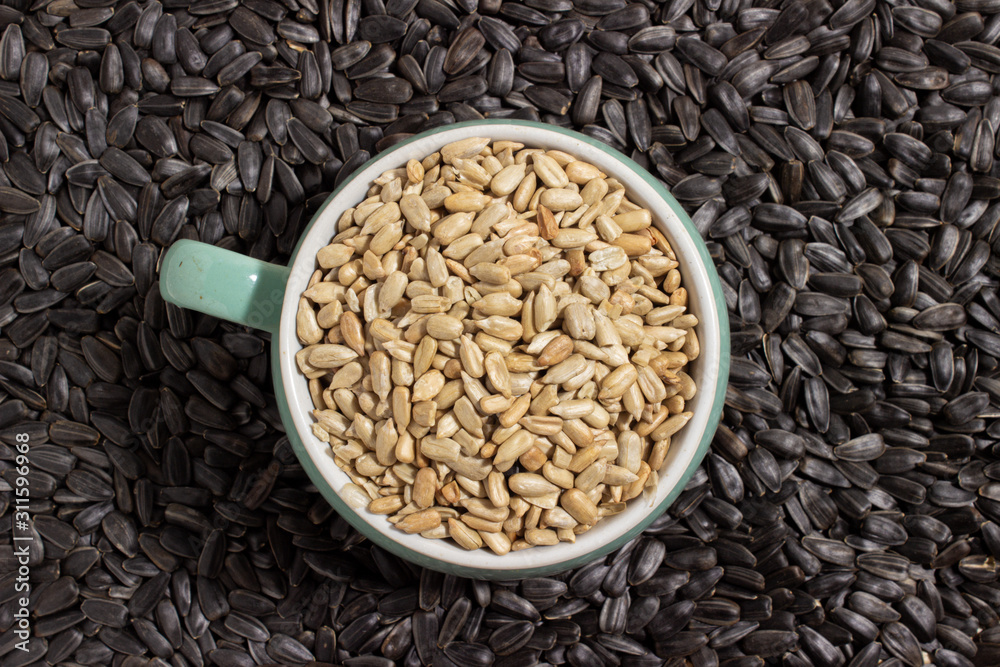 peeled sunflower seeds sprinkled in a small colored bowl on a background of unpeeled black sunflower seeds peeled sunflower seeds sprinkled in a small colored bowl on a background of unpeeled black sunflower seeds