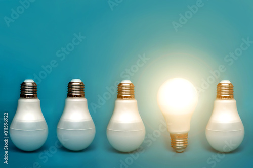 Among others, a bright light bulb shines. conceptual ideas and ideas. stands out among others. a bright lamp shines