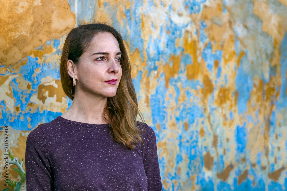 Obraz premium Portrait of a beautiful mature woman looking away over a an old wall background, pensive, thoughtful.