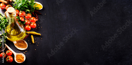 Food background. Top view of olive oil, cherry tomato, herbs and spices on rustic black slate. Colorful food ingredients border.