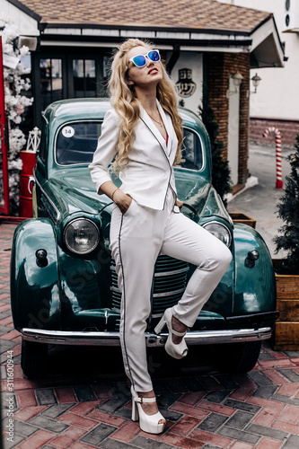 Fashion photo. Model in a white pantsuit posing near a green retro car.