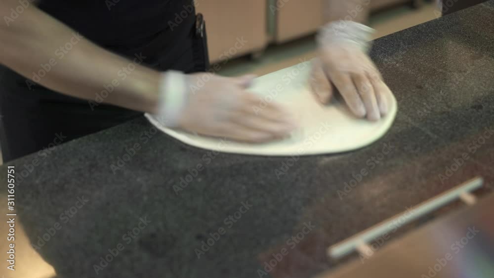 Top view handheld shot of cook in white rubber gloves stretches pizza dough on the marble kitchen table. Cook prepares wheat flour for pizza Top view handheld shot of cook in white rubber gloves stretches pizza dough on the marble kitchen table. Cook prepares wheat flour for pizza