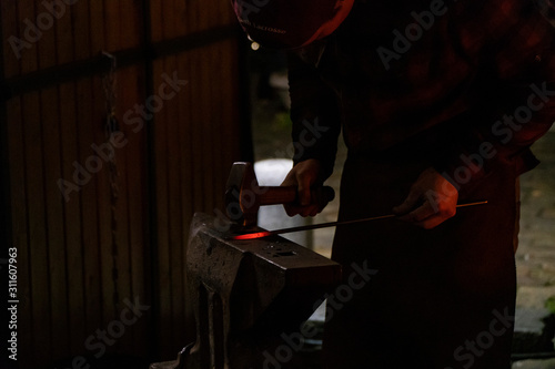 Blacksmith working on metal on anvil at forge