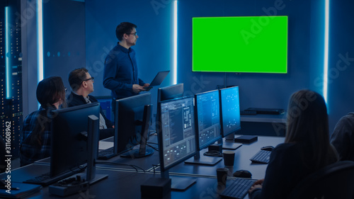 Team of Professional IT Developers Have a Meeting, Speaker Talks about About New Concepts, On Wall TV has Green Mock-up Screen. Concept: Software Development, Deep Learning, Artificial Intelligence