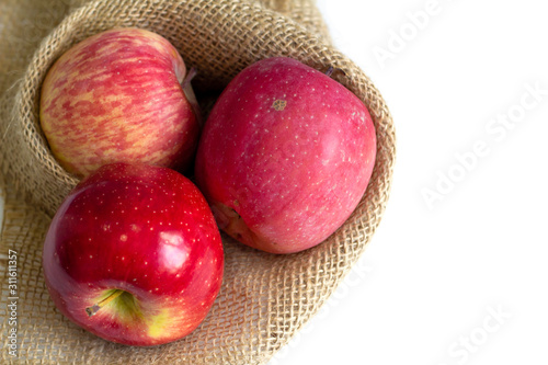 three red apples on the table in sackcloth package on white background 