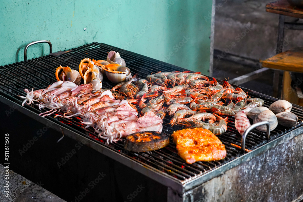 Delicous seafood grilling on ember stove close up. Street food at night in Vietnam.