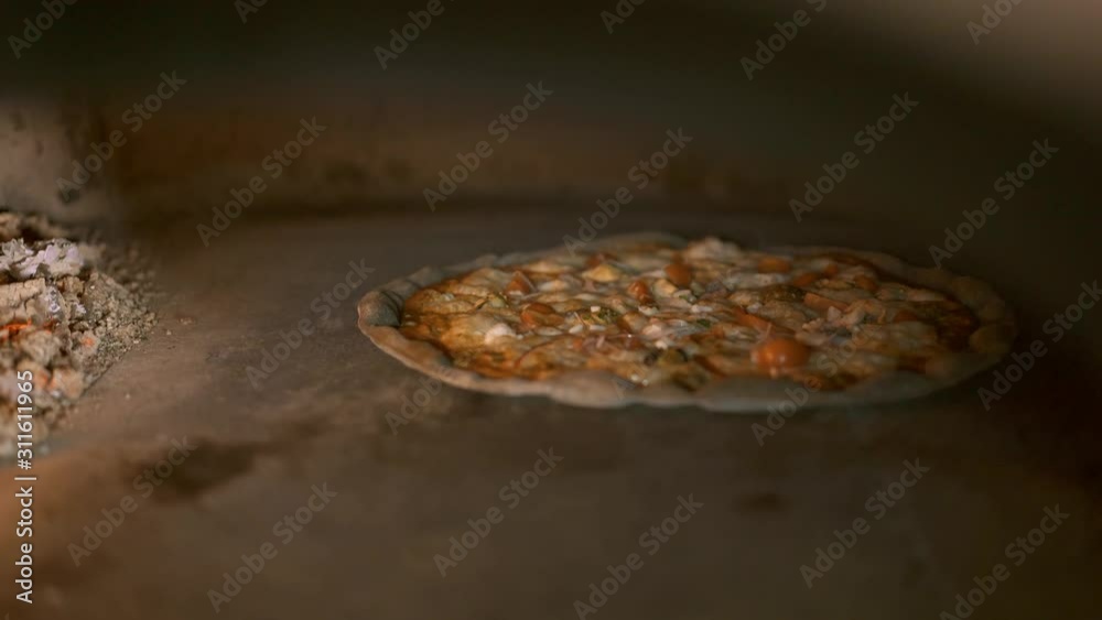 Handheld shot of seafood pizza baking in the oven beside coals and fire