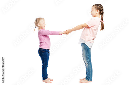 Little smiling girls with pigtails in jeans and pink sweaters hold hands. Full height. Isolated over white background.