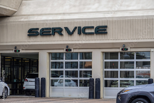White cars entering an automobile service center garage through an open garage door. Two other doors are closed