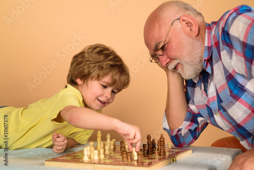 Kid boy playing chess with grandfather. Chess competition. Grandfather and grandson playing chess. Grandpa and grandson playing chess spending free time together. Brain development and logic concept.