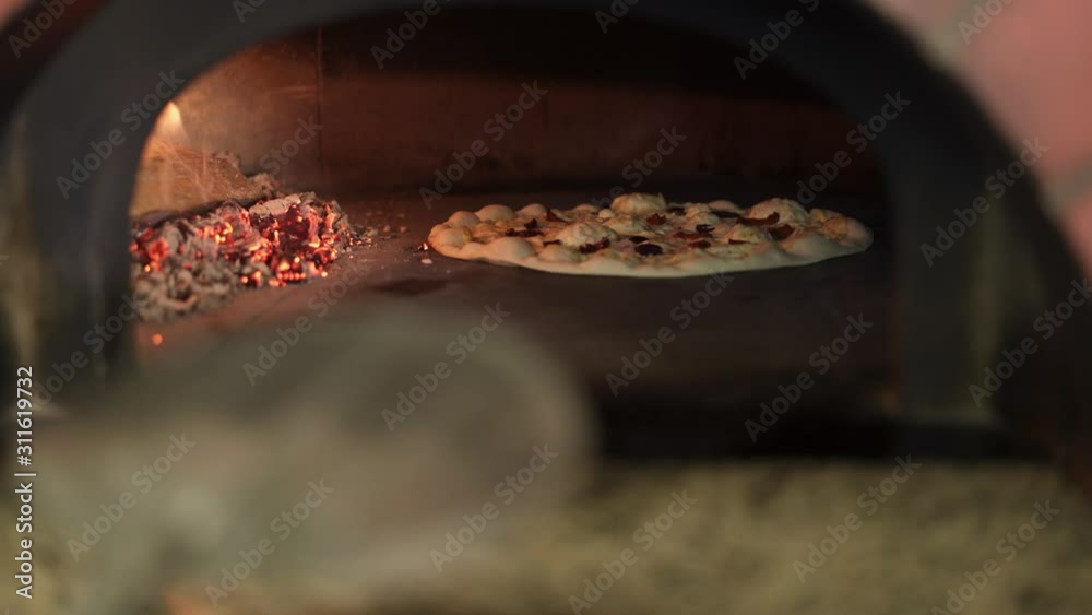 Handheld shot of cook twisting pizza inside the oven. Vegetarian pizza