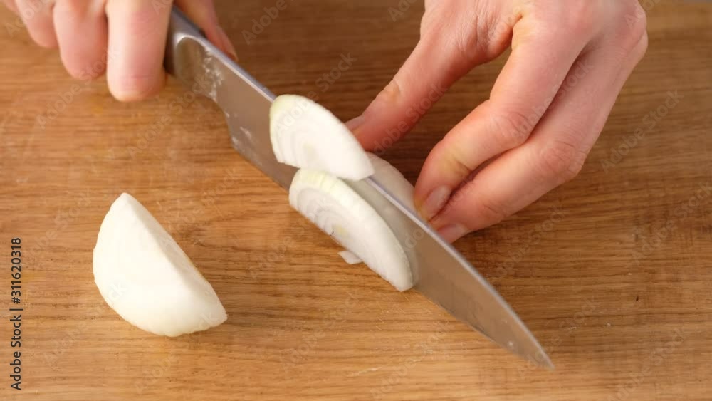 Female hands cut an onion into pieces on a cutting board close-up. Making soup. Female hands cut an onion into pieces on a cutting board close-up. Making soup.