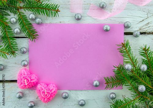 It's time for a holiday! Festive blank pink greeting card on white wooden background with decorative ribbon, pink candles and green Christmas tree. Top view.