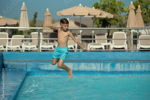 Caucasian boy having fun making fantastic jump into swimming pool at resort.