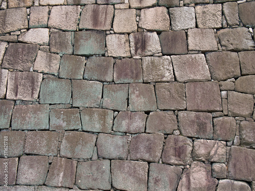 Natural rock blockwork in a wall with green and lilac colours caused by algae and lichen growth - suitable for a graphical background.