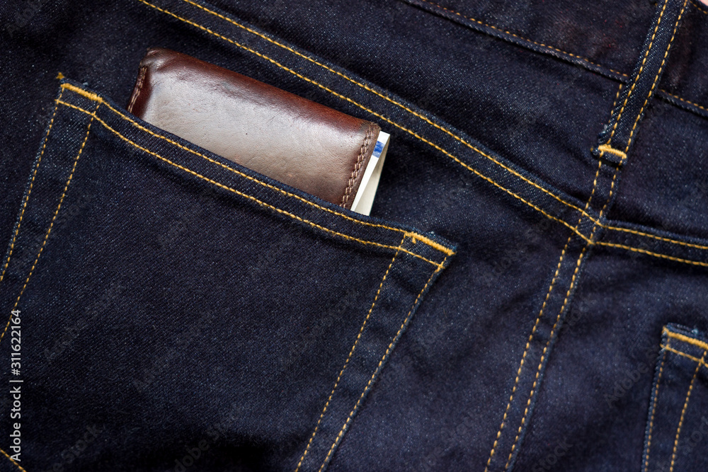 Wallet and usd banknote showing in back pocket of jeans. Selective focus on the edge of the wallet.