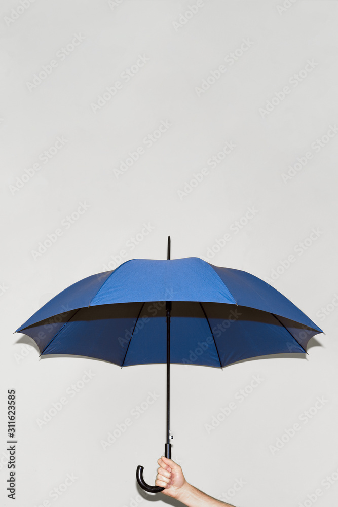 A man holds a blue umbrella in his hand against a gray wall. Open space above the umbrella. Concept autumn, color of the year 2020, business, protection.